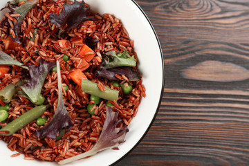 Tasty brown rice with vegetables on wooden table, top view