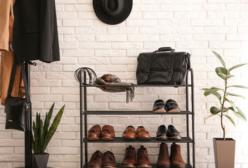 Shelving rack with stylish shoes and accessories near white brick wall indoors