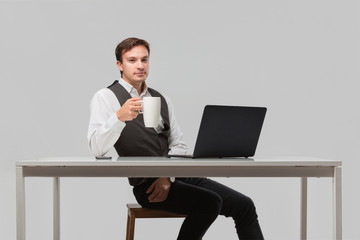 Successful man in a white t-shirt and grey vest drinking coffee sitting at the white table