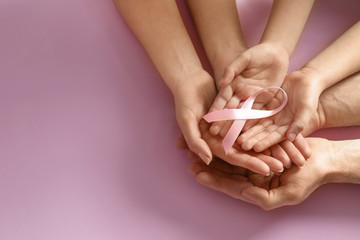 Family holding pink ribbon on color background, top view with space for text. Breast cancer...