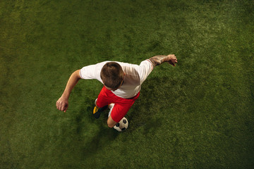 Top view of caucasian football or soccer player on green background of grass. Young male sportive model training, practicing. Kicking ball, attacking, catching. Concept of sport, competition, winning. © master1305