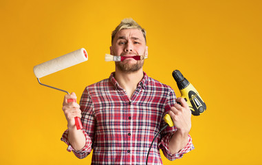 Multitasking problem. Desperate repairman holding perforator, paint roller and brush simultaneously