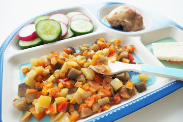 .balanced baby food: stewed vegetables, fried chicken, chopped vegetables and bread rolls arranged in different sections on a plate. Bamboo tableware plate and fork..