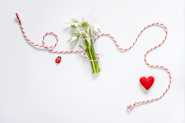 Bouquet of delicate snowdrops on white background with red and white rope and red felt heart. First...