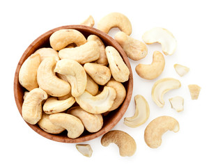 Cashew nuts in a wooden plate and scattered on a white background. View from the top