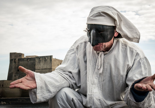 Pulcinella traditional Neapolitan mask gestures with Castel dell'Ovo in the background in the Gulf of Naples.