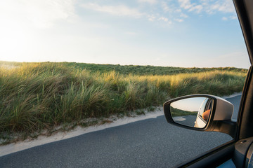 Car window view with grassy dunes and road on Sylt island