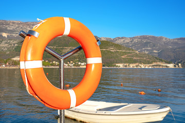 Closeup orange lifebuoy on a background of a boat in a marina swinging on the waves in the sea on a...