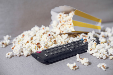 The cardboard box with popcorn and remote control on grey background. Concept of hobby or pleasant time spending at home, watching movie. Indoors.