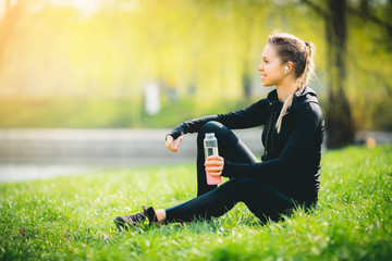 young pretty thirsty blonde Caucasian girl in suit resting after sport run in the football stadium...