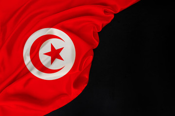 Tunisia state silk national flag folded in soft folds on black blank form, concept of tourism, economy, politics, emigration