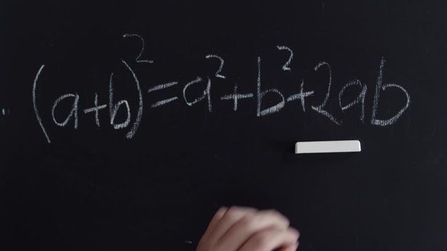 A man's hand writes a mathematical formula with chalk on a blackboard. Formula for reduced multiplication with chalk on a blackboard