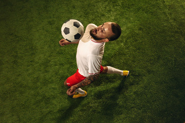 Top view of caucasian football or soccer player on green background of grass. Young male sportive model training, practicing. Kicking ball, attacking, catching. Concept of sport, competition, winning.