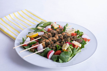 shrimp on sticks and vegetables in a white plate on a table