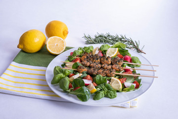 shrimp dinner on sticks and vegetables in a white plate on a table