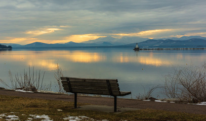 bench on Lake Champlain water front with view of vibrant sunset and the New York Adirondack mountains in winter 