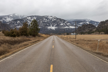 Empty roadway between grass fields leading to snow covered mountain range