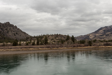 Short rolling hill behind calm green river on overcast day