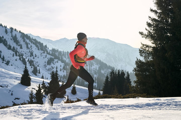 Trail runner in pink jacket woman running in winter mountains trail on snow.