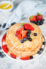 A stack of crepes lies in a plate, decorated with berries on a gray concrete background