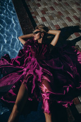 Luxury woman lies near bassin in red dres.