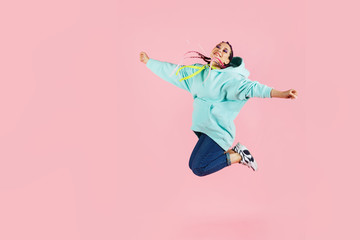 Beautiful young fit dancer in blue hoodie dancing and jumping isolated on pink background