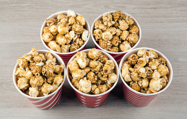 five red cardboard cup in a row with sugar popcorn on a wooden table