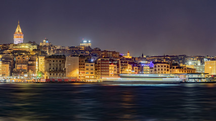 Fototapeta na wymiar city lights illuminating Istanbul at night and a ship passing through the Golden Horn and Galata tower, long exposure, wavy estuary, street lights, high quality