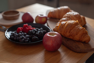 Big croissants, berries, red apples on a wooden table