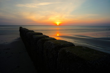 Sonnenuntergang am Meer mit dunklen Steinen im Vordergrund