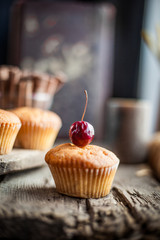Muffin with a cherry on top. Beautiful cupcake on a wooden background in rustic style. Cooking, dessert. Muffins close-up, homemade cake.