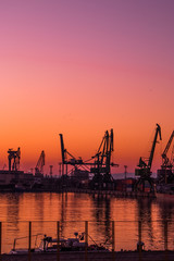 Sunset on cargo export and import port with cranes silhouette from industrial and transportation, trade port on business city