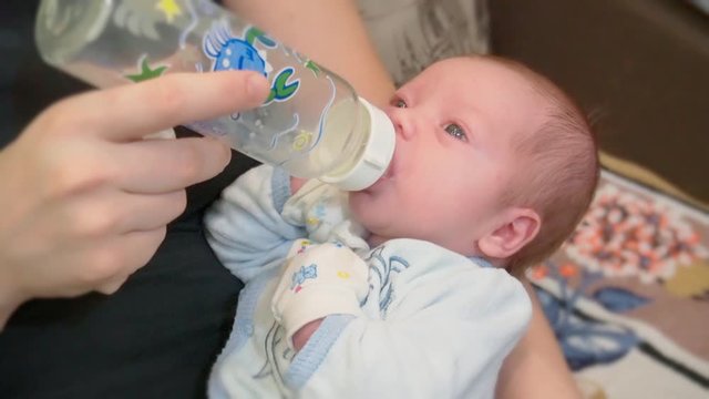 Mother holding and feeding baby from milk bottle. Portrait of cute newborn baby being fed by her mother using bottle. Loving woman giving to drink milk to her son. Mother feeding her baby.