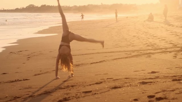 Beautiful girl in swimsuit doing cartwheel during sunset by the ocean