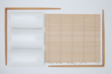 Top View Of White Empty Sushi Plates With Bamboo Chopsticks and Mat.