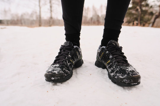 Close-up of unrecognizable person in winter black sport shoes standing on snow