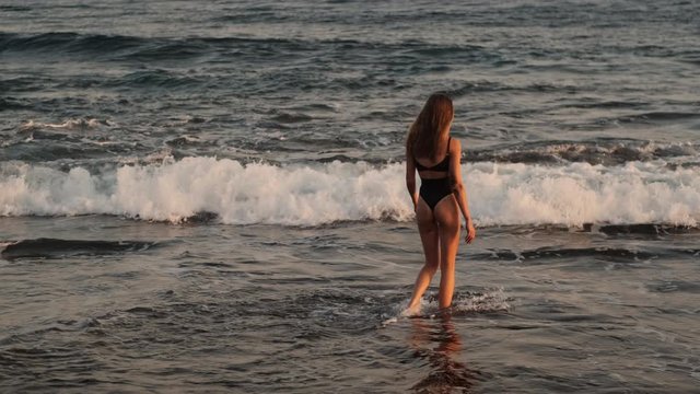 Back view shot of attractive girl swimming in ocean resting on tropical island