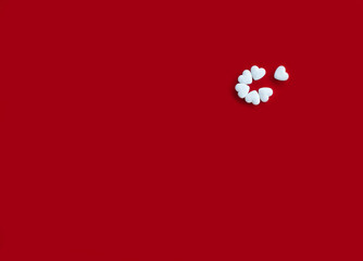 White heart-shaped pills on red background with empty place for text, top view. Several tablets are collected in a flower without one piece.