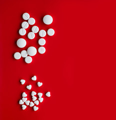 White large and small pills in the shape of a heart on a red background with empty place for text, top view