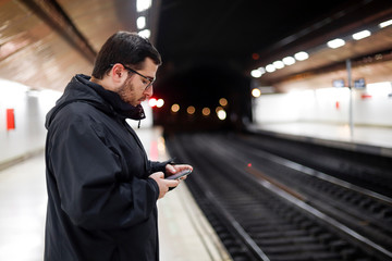 young adult looking on his smartphone on a empty metro station