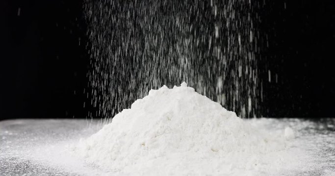 Pile of white flour falling on black background. 4k resolution, slow motion
