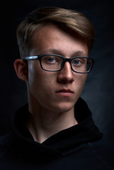 Fototapeta na wymiar Smart teenager with short hair and glasses an black background. Strong and handsome face.
