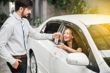 Car dealership. The woman receiving car key with a smile from the salesman. Auto Leasing Business.