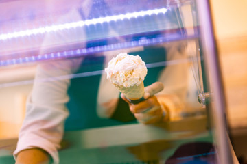 Gelato Italian Ice Cream seller puts a scoop of Gelato in a cone on her hand with Gelato spade.
