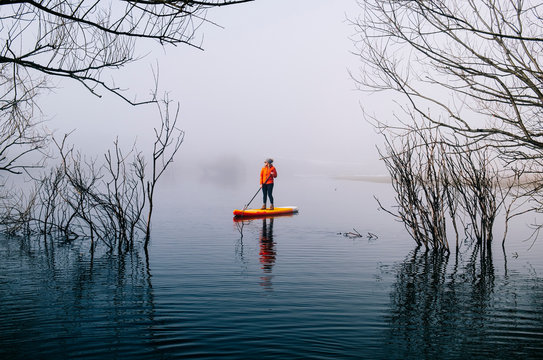 Woman stand up paddle surfing on a lake in the fog