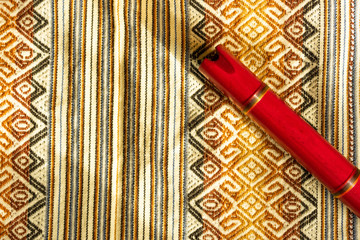 Top view of Peruvian flute. Quena. Above a colorful Peruvian textile, with space on the left side of the image. Concept of traditional instruments.