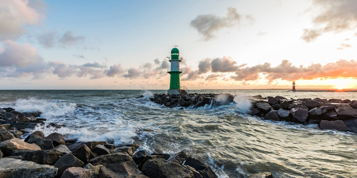 Germany, Mecklenburg-West Pomerania, Warnemunde, Lighthouse and sea waves crashing against rocks at sunset