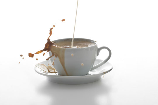 Milk Splashing In A Cup Of Coffee In Front Of White Background