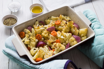 Vegetables cauliflower onion carrots baked in the oven on a white pan, olive oil and herbs and spices. Concept spring diet menu. Close up