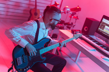 Create music and a recording studio concept - Bearded funny man guitarist recording electric bass guitar track in home studio